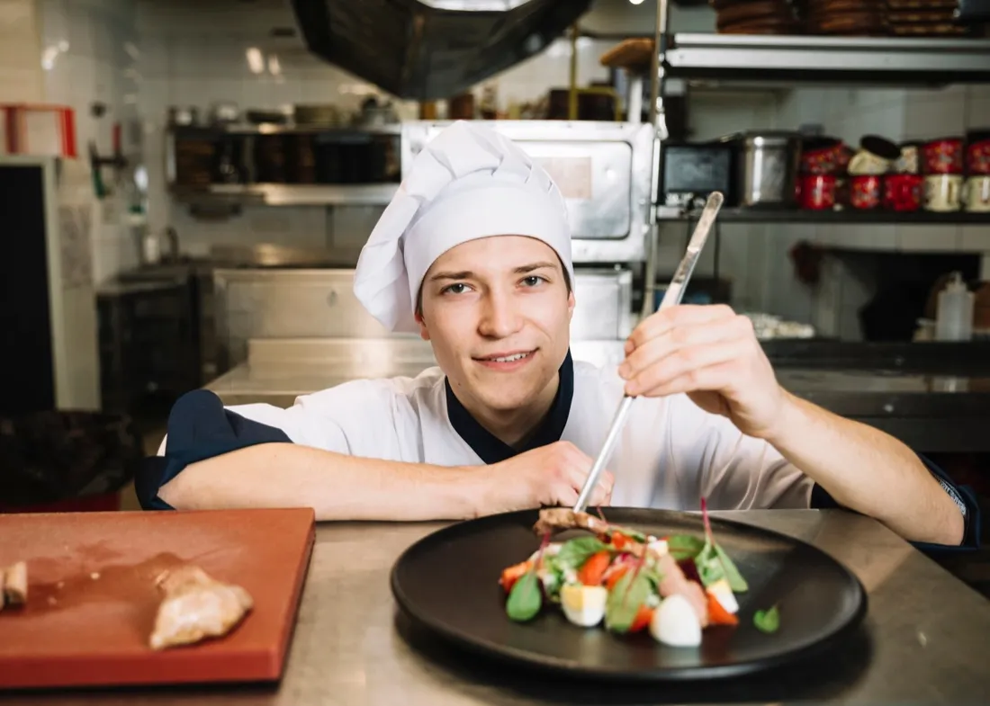 A chef in whites plating a dish with tweezers in the restaurant kitchen
