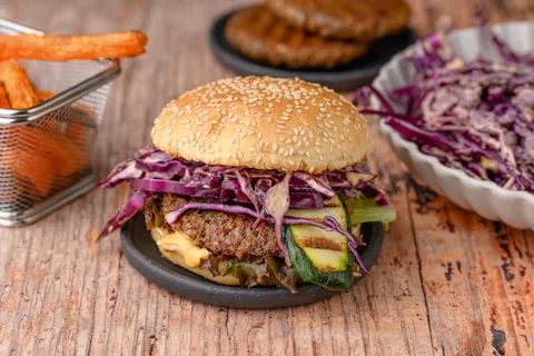 Burger with red cabbage slaw on a dark plate, fries alongside