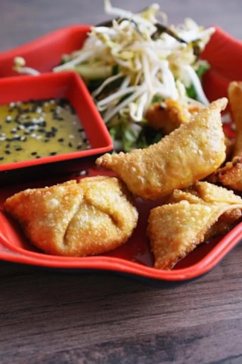 Fried cheese wontons on a red plate with dipping sauce