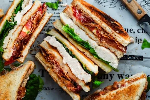 Toasted chicken club sandwiches cut into quarters on newspaper