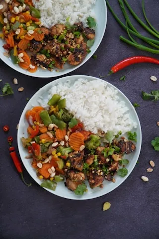 Two plates of chicken and vegetable stir-fry with rice and chillies