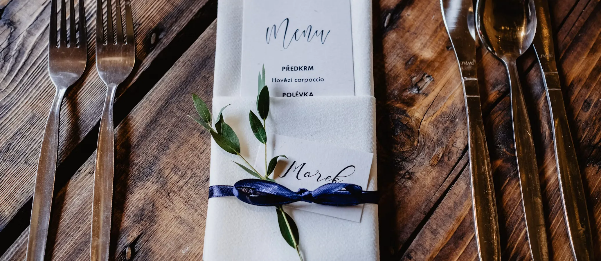 A folded napkin holding a handwritten menu card, laid on a rustic wooden table between cutlery