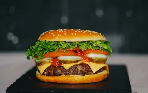 Cheeseburger with lettuce, pickles and tomato sauce on a slate board