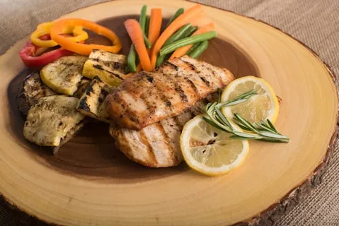 Grilled chicken breast with lemon, rosemary and vegetables on a wooden platter