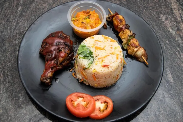 Roast chicken leg, satay skewers and rice on a dark plate